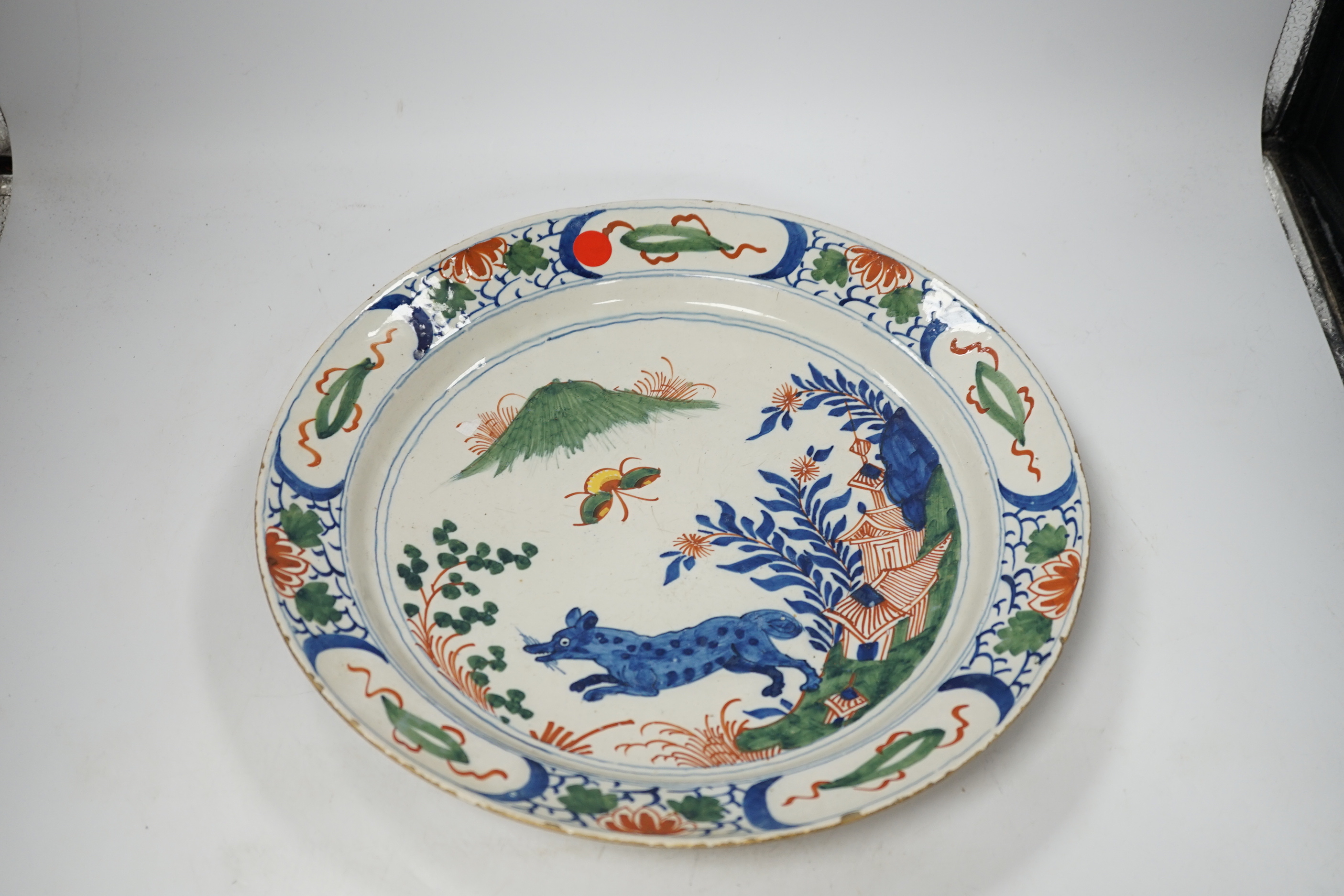 An 18th century delftware dish, the centre painted with a wolf, a bee and a pavilion, 35cm